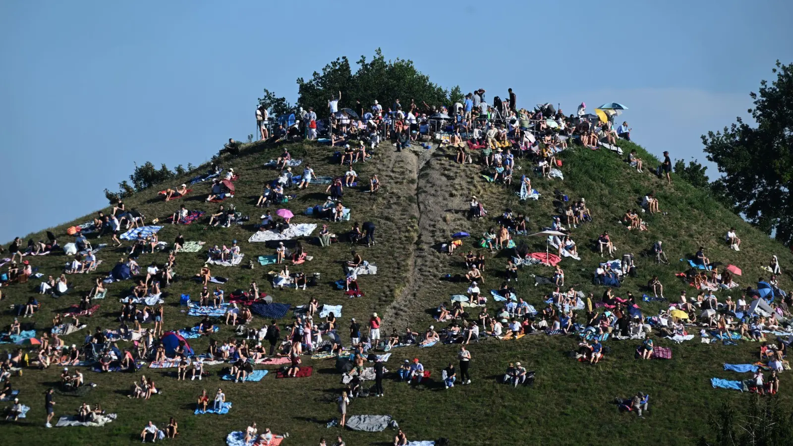 Erste Besucher bevölkern den Olympiaberg im Münchner Olympiapark, um von dort die partielle Sonnenfinsternis zu beobachten. (Bild: Felix Hörhager/dpa)