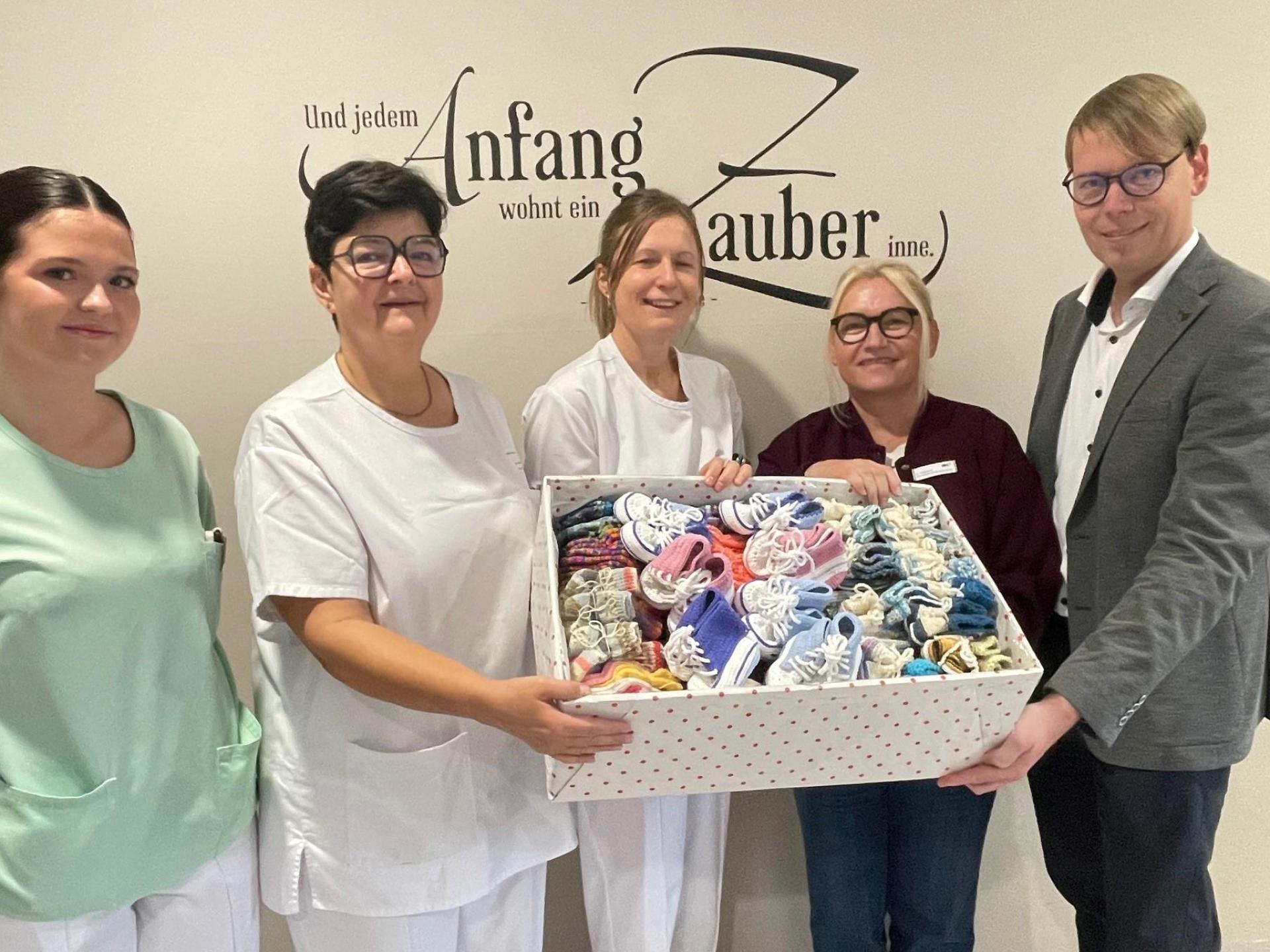 Burgi Zielbauer (Zweite von rechts) überreichte eine Kiste mit 220 Paar gestrickten Söckchen und Schühchen an die Station 32 des Klinikums Weiden. Darüber freuen sich Klinikdirektor Stephan Schumacher (rechts) sowie (von links) Schwesternschülerin Lara Trinkner, stellvertretende Stationsleiterin Jacqueline Kleber und Oberärztin Dr. Ines Erhardt. (Bild: Friedrich Peterhans, KNO)