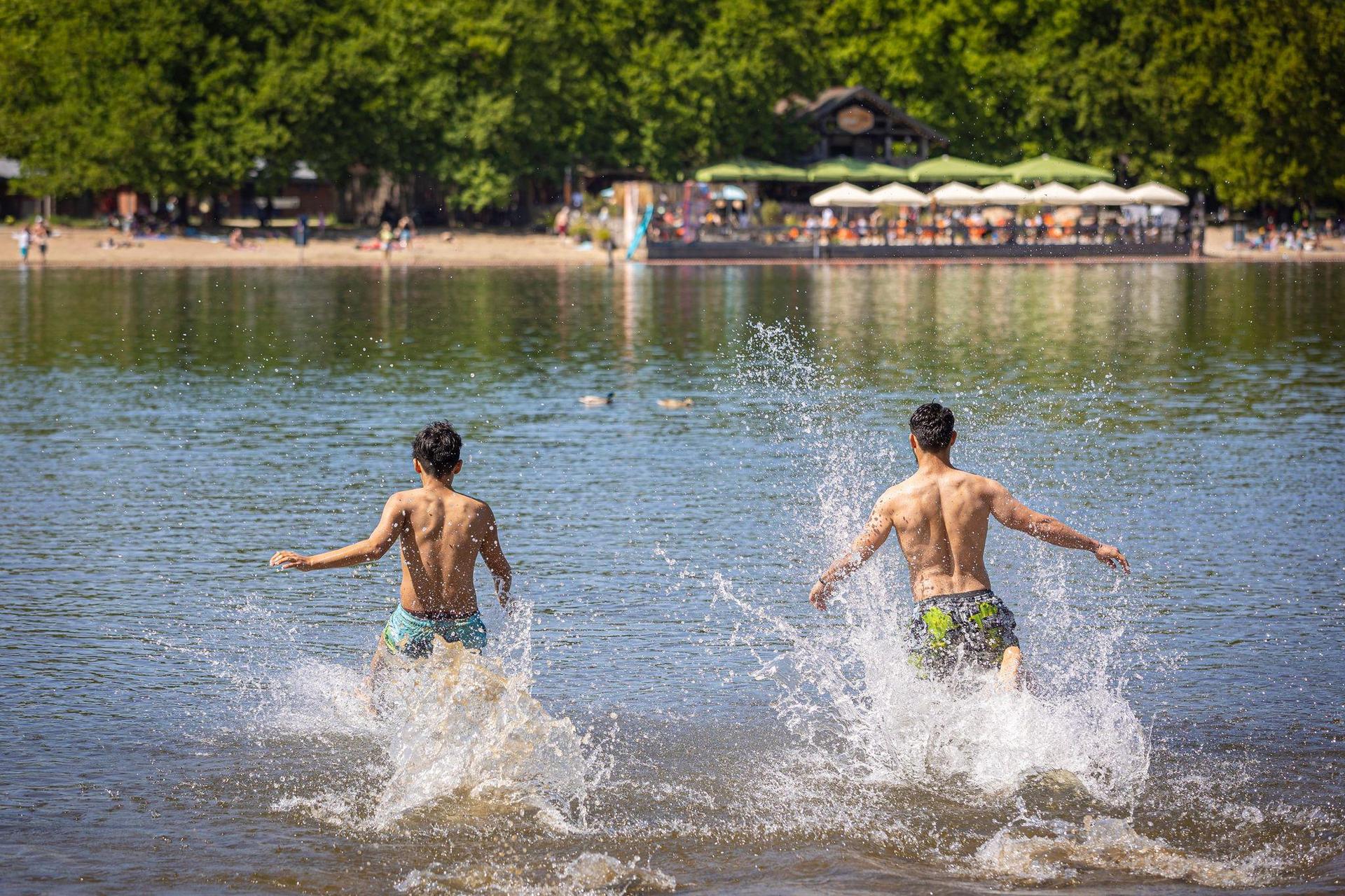Zwei junge Männer rennen bei sonnigem Wetter in das Wasser eines Sees. (Bild: Moritz Frankenberg/dpa/Symbolbild)
